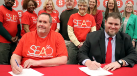 Members of the SEA stand for the signing of a new agreement which results in an increase in teacher pay scales in the district.