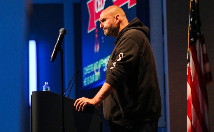 U.S. Senator John Fetterman (D-Pa.) speaks at a lectern wearing his trademark Carhartt hoodie-shorts combo.