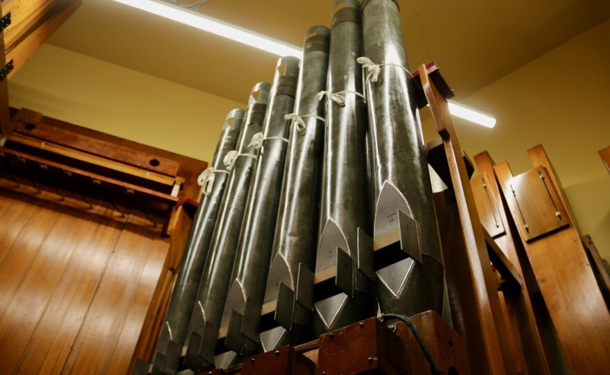 The pipes of a nearly century-old organ extend to the ceiling of a small room with wood paneling.