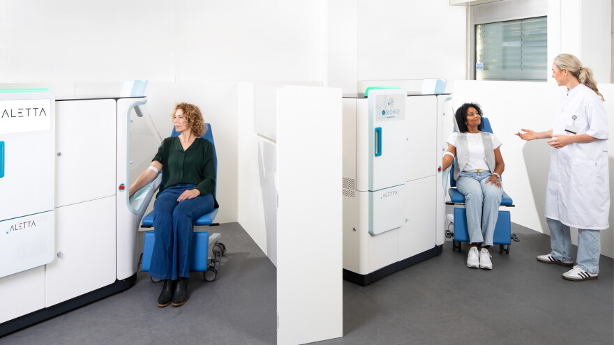  two large machines  in action drawing blood from two patients while one lab worker supervises.   