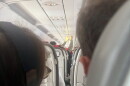 A passenger holds an IV saline bag above the aisle as medical volunteers respond to an in-flight emergency aboard a flight approaching Ben Gurion Airport near Tel Aviv, Israel, on October 17, 2026. The aircraft encountered turbulence as passengers and crew worked to stabilize a woman experiencing difficulty breathing.