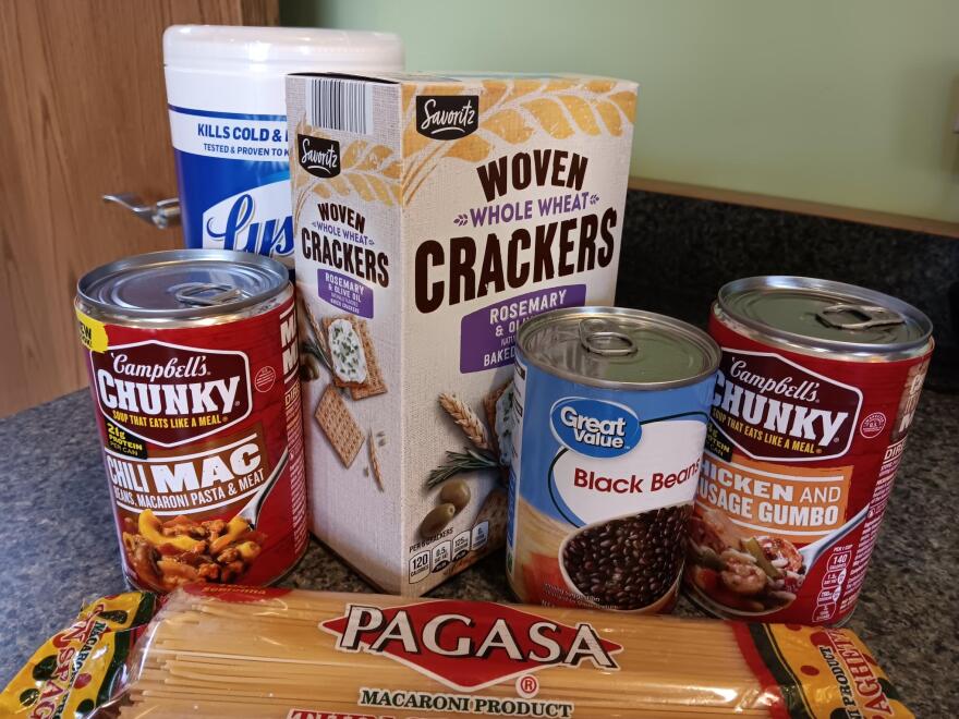 A collection of soup, pasta, crackers and cleaning wipes sits on a countertop.