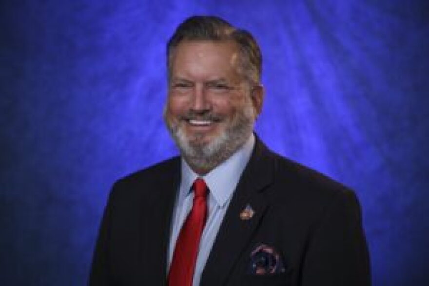 Head shot of a man with a gray beard, wearing a dark suit