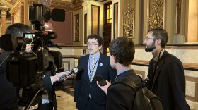A man wearing a suit speaks with other men in suits holding microphones.