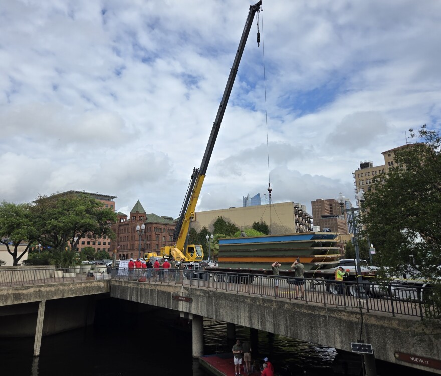 Crane lifts barge off flatbed truck and lowers them into the San Antonio River at the East Nueva Street bridge on April 10, 2026