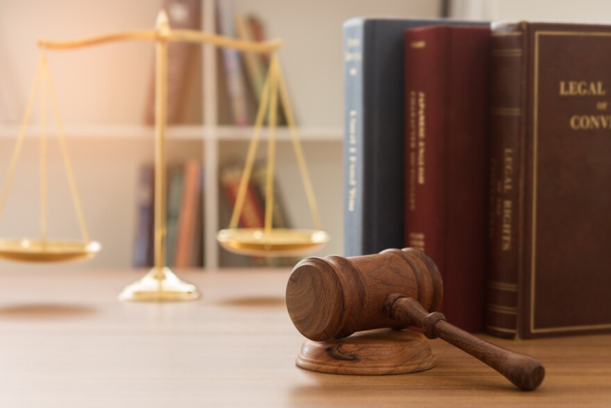 A photo of a judge gavel, a scales of justice, and law books on a desk. 