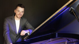 Peter Dugan stands leaning against an open piano