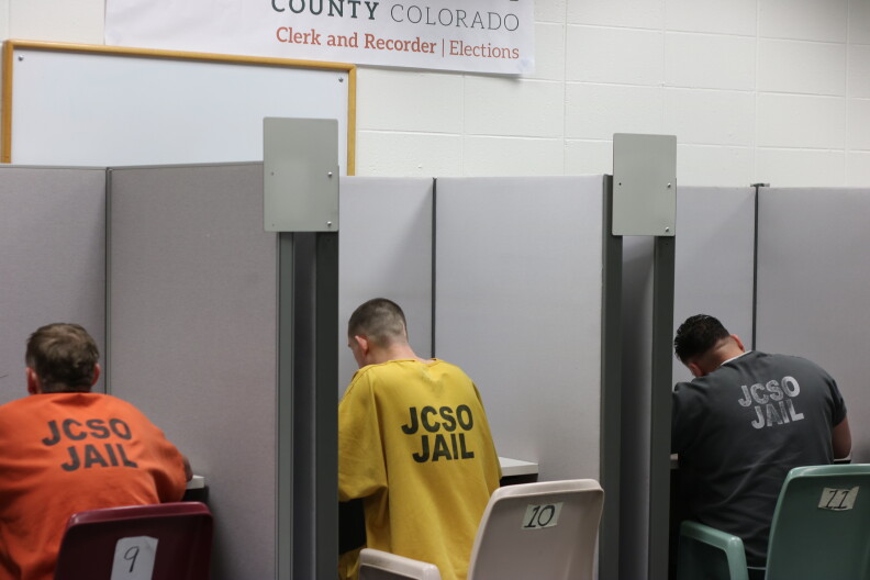 Three inmates in orange, yellow and gray uniforms vote in booths at the Jefferson County jail. 