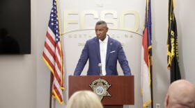 Sheriff Bobby Kimbrough behind a podium speaking at a press conference with three flags behind him. 