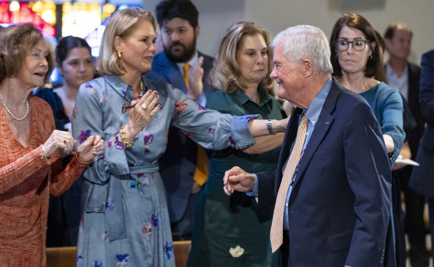 A man wearing a suit is greeted by a group of women in a church. One reaches out to touch him on the shoulder.