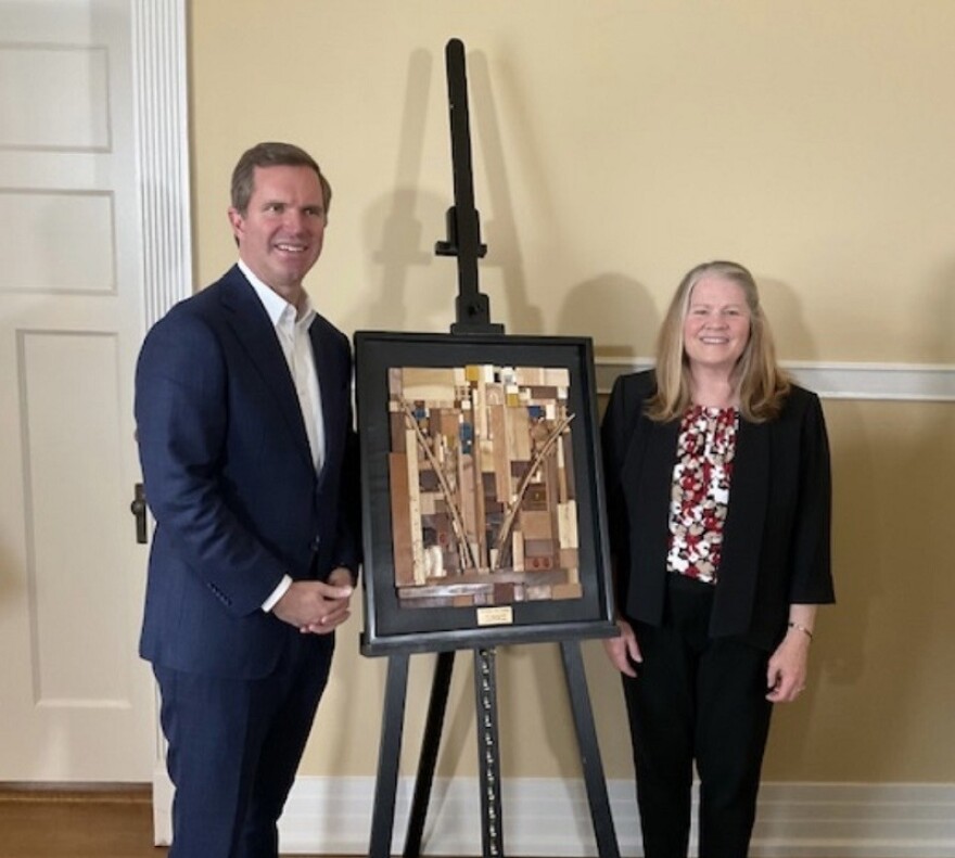 Governor Andy Beshear stands by artist Aleta Stone and one of the collage art awards.
