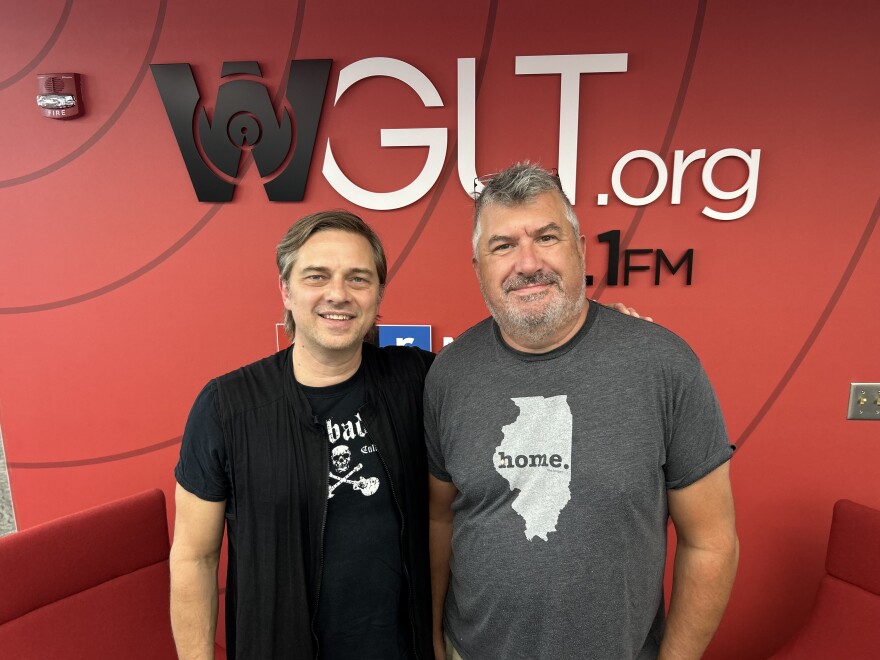 Two band members in front of a radio station logo. 