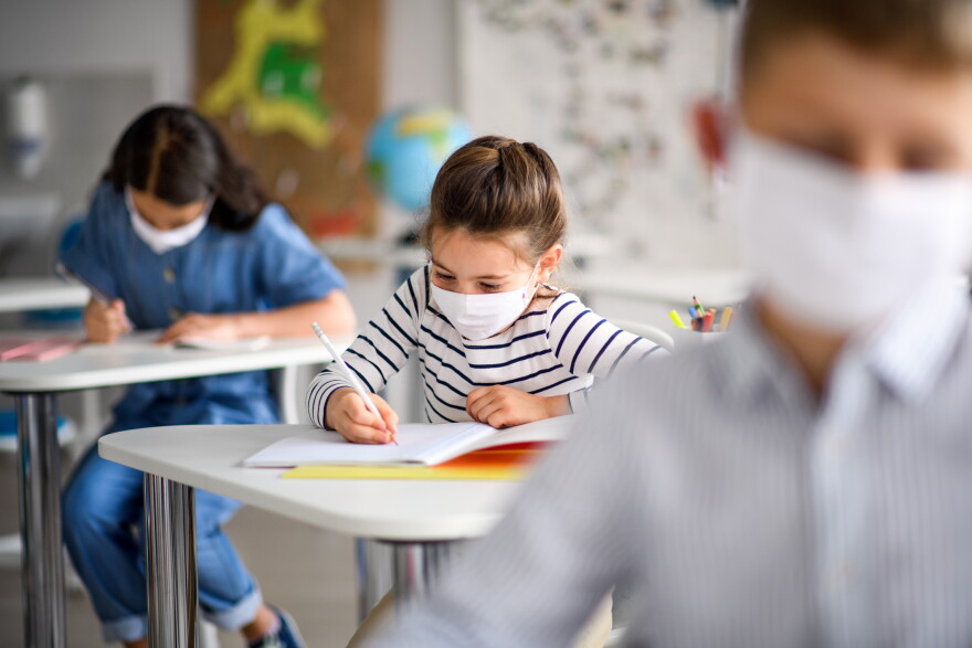 Children with face masks in a school classroom.