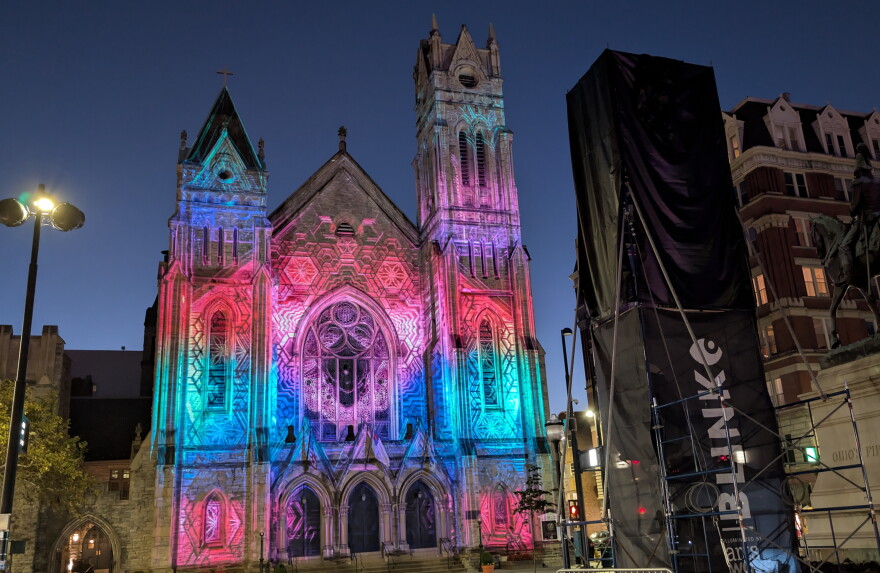 Colored lights cover the facade of a church at dusk.