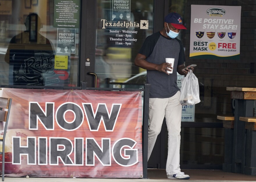 A man walks by a "Now Hiring" sign. 