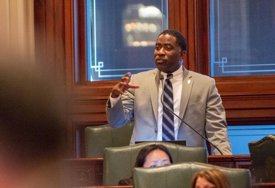 Man in a suit speaking into a microphone in a legislative chamber