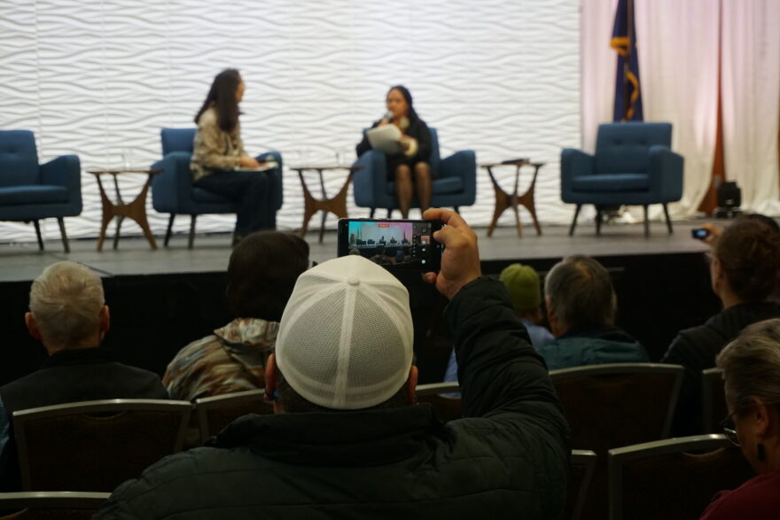 An audience member records the U.S. Senate candidate forum held on Friday at the Alaska Federation of Natives convention in Anchorage. On the left, former U.S. Rep. Mary Peltola, a Democrat challenging U.S. Senator Dan Sullivan, is the only candidate on the stage. Sullivan did not attend. Seated next to Peltola is journalist Antonia Gonzalez, who served as the moderator.
