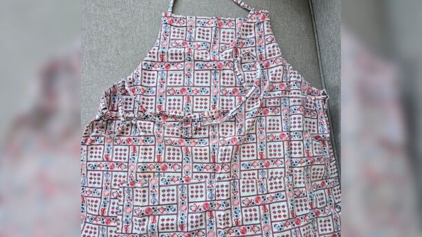 An apron with a strawberry and teapot pattern against a gray background.