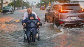 Victor Corone, 66, pushes his wife Maria Diaz, 64, in a wheelchair through more than a foot of flood water on 84th street in Miami Beach on Wednesday, June 12, 2024. Diaz had a doctor’s appointment, and they had to ditch the car in the parking lot on Collins Ave and walk more than 20 minutes to get home.