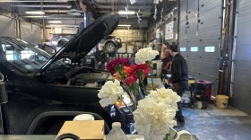 A vase of carnations in front of a car with hood open in a mechanic shop