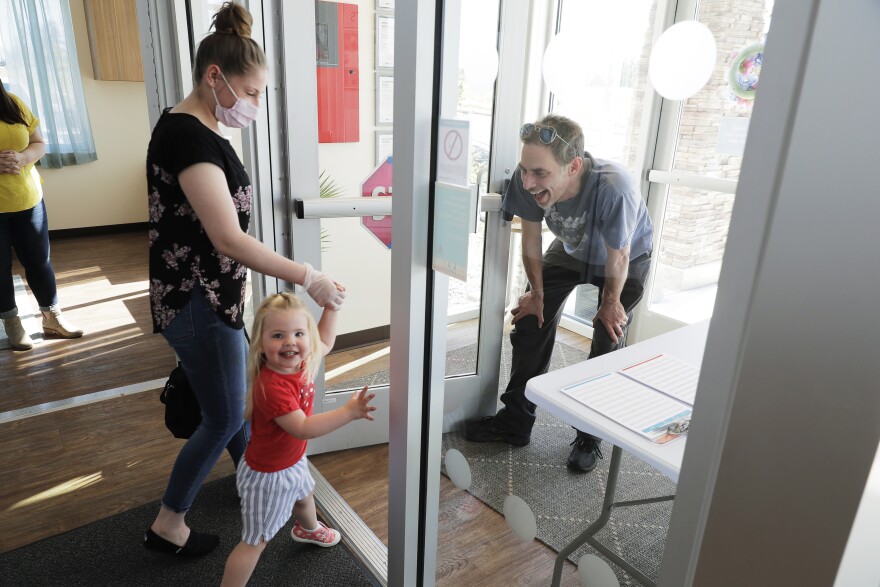 In this May 27, 2020 photo, Samantha Sulik, left, director of the Frederickson KinderCare daycare center, in Tacoma, Wash., looks on as Michael Canfield, right, waits in an entryway to pick up his daughter Aurora at the end of the day.