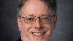Studio portrait of a smiling man with glasses.