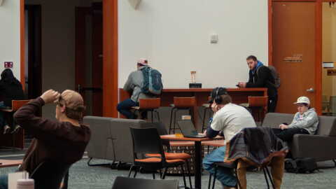 Students sit by themselves at separate tables and couches in a lounge area.