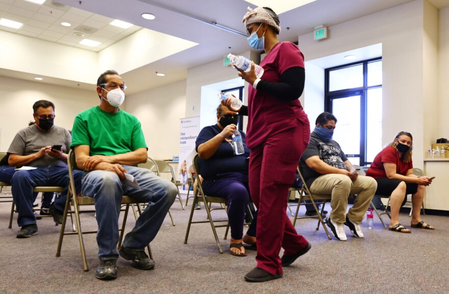 A healthcare worker passes out water to people waiting in the observation area after receiving a dose of a COVID-19 vaccine at a vaccination clinic hosted by Providence St. Mary Medical Center in Apple Valley, California.