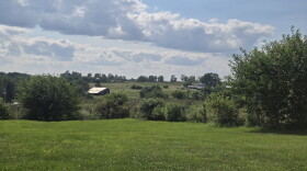 A rural landscape with trees, rolling fields and barns
