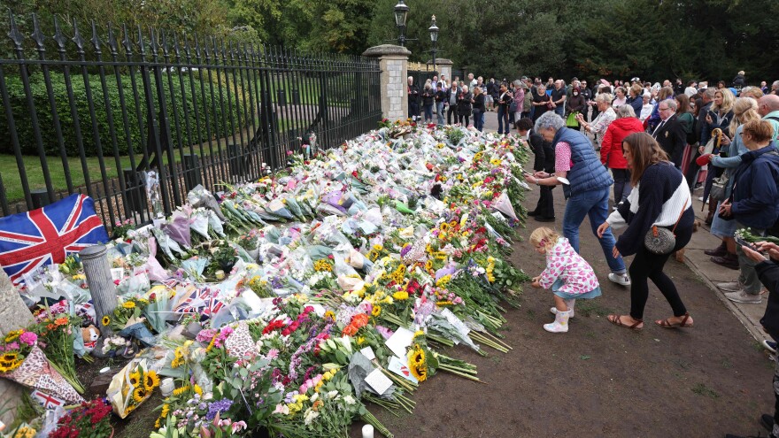 Members of the public leave floral tributes at the Cambridge Gate, the entrance to the grounds of Windsor Castle, on Friday, after Queen Elizabeth II died at the age of 96.