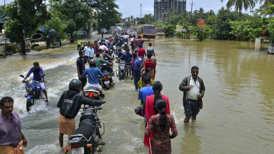 People move past a flooded road in the southern Indian state of Kerala, where monsoon rains have destroyed roads and left hundreds of thousands of people homeless.