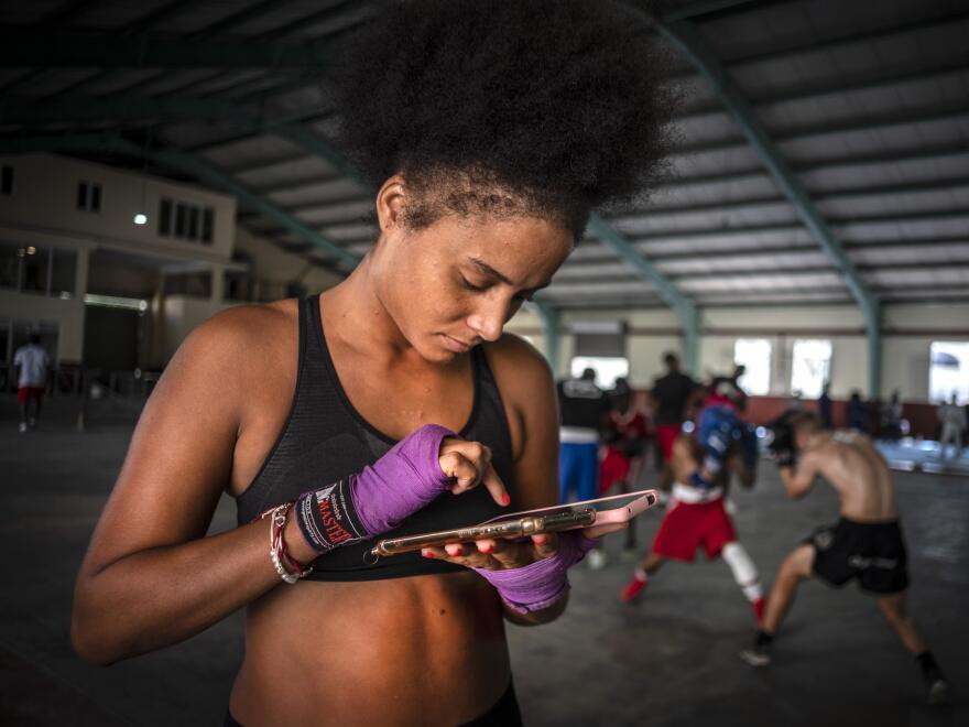 Dic.  La boxeadora Giselle Bello García envía un mensaje de texto a un teléfono móvil mientras otros atletas entrenan en un gimnasio de boxeo en La Habana, Cuba, el lunes 5 de mayo de 2022.