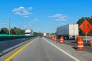Trucks and SUVs travel a highway under construction, lined with barrels and a concrete divider 