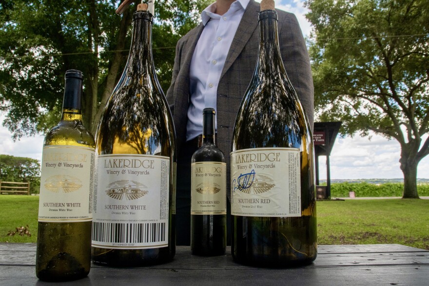 Slupe stands behind a collection of wine bottles in his winery. A standard one contains about 5 glasses worth of wine and varies from 11.5 to 13 inches in height. A 6-liter bottle typically is 22 inches tall and equals eight standard ones or 40 glasses of wine. (Zoey Thomas/WUFT News)