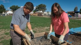 A man and a woman look into a box that holds a screen with mud on it.