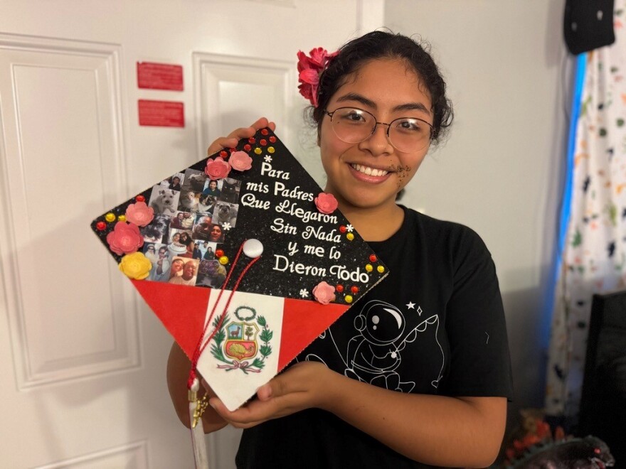 Dayana, a recent McLane High School graduate, shows off her graduation cap. Behind her, red cards are taped on the front door of her and her father’s apartment.