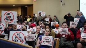 People in city hall chambers hold posters that say no data center 