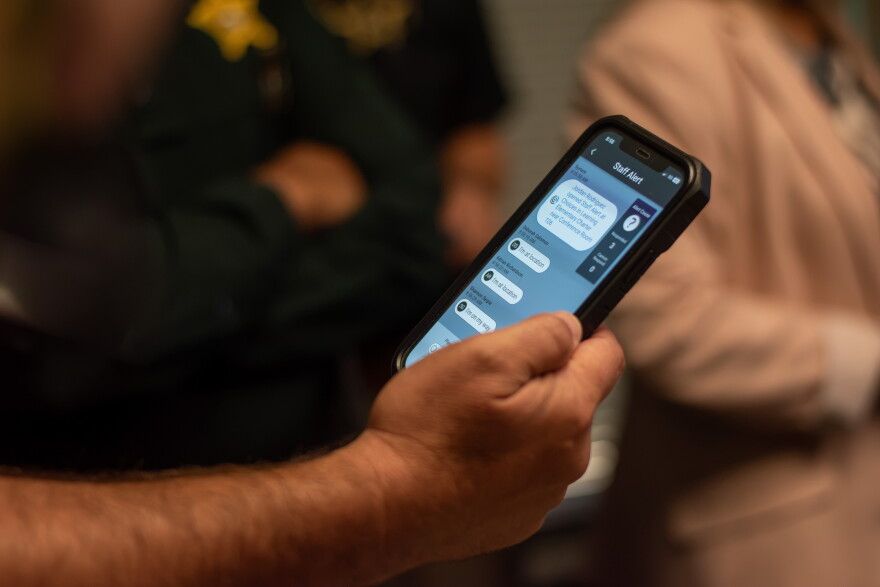 A law enforcement officer receives an alert notification on a phone, showing the location of the emergency on the school campus.