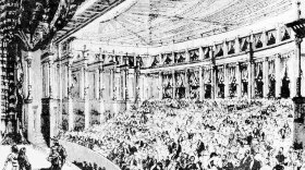 Sketch of an audience in a large theater watch a performance. The actors on stage are dressed in Viking hats and cloaks. 