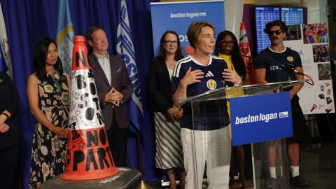 Boston Mayor Michelle Wu and a host of Massachusetts and Scottish officials look on as Massachusetts Gov. Maura Healey lauds a traffic cone at Logan Airport (Robin Lubbock/WBUR)