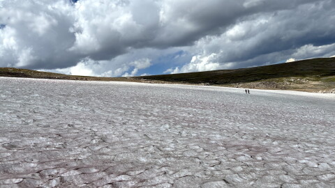Two researchers stand on a vast ice patch in Wyoming’s Beartooth Mountains beneath large, dark clouds.