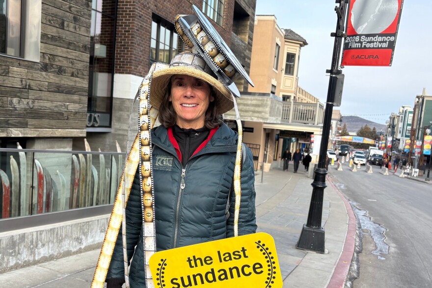 A woman wearing a film reel on her head holds a sign that reads "the last sundance" while attending final Sundance Film Festival in Park City, Utah, on Friday, Jan. 23, 2026, before the festival moves next year to Boulder, Colo.