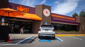 A parking attendant takes shelter under an umbrella during a lull in early voting at the Orange County Supervisor of Elections office on Monday, Aug. 10, 2026.