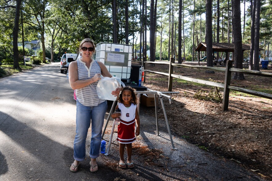 Mother and daughter use jugs to collect safe water - the same quality standard accepted by DEHC - from Water Mission tap stands in Columbia.
