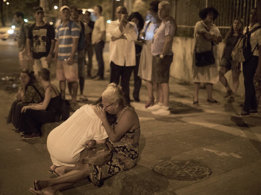 People cry on the sidewalk next to the scene where council member Marielle Franco and her driver were shot to death by two unidentified attackers in Rio de Janeiro on Thursday.