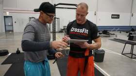 Two ment stand in a gym near weights and other workout gear