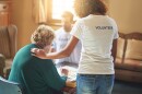 A young woman wearing a volunteer T-shirt speaks to an older woman who is playing a board game.