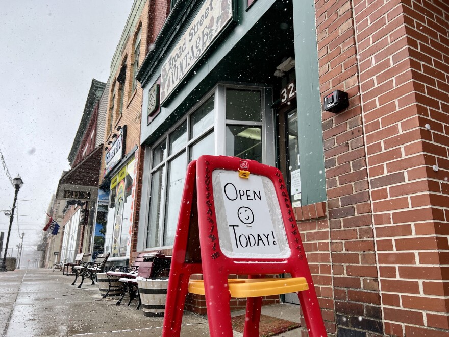 A sign on a child-sized easel reads, "Open Today!" It sits on a sidewalk outside a row of shops in Newton Falls.