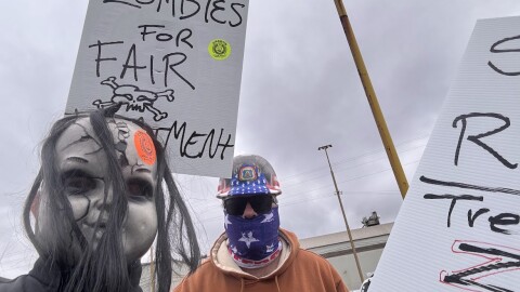 A picketer is seen with a scary doll mask. Another protester holds a sign that says "zombies for fair treatment." 