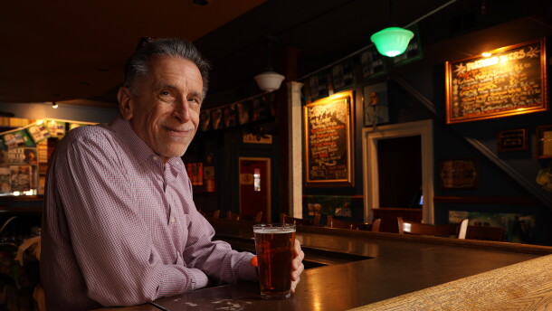 A man sits at a bar in a dimly-lit room with a pint.